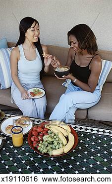 Stock Photo - women sit side 
by side on a sofa 
eating a healthy 
breakfast. fotosearch 
- search stock 
photos, pictures, 
images, and photo 
clipart