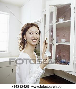 Stock Photograph - woman in a kitchen 
removing a fragile 
looking teacup 
from a cabinet. 
fotosearch - search 
stock photos, 
pictures, images, 
and photo clipart