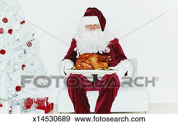 Stock Photograph - father christmas 
sitting next to 
a christmas tree 
holding a roast. 
fotosearch - search 
stock photos, 
pictures, images, 
and photo clipart
