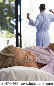 Stock Image - mature woman lying 
in bed, mature 
man stretching 
by window. fotosearch 
- search stock 
photos, pictures, 
images, and photo 
clipart