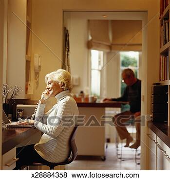 Stock Photo - senior woman using 
computer and telephone, 
senior man in 
background. fotosearch 
- search stock 
photos, pictures, 
images, and photo 
clipart