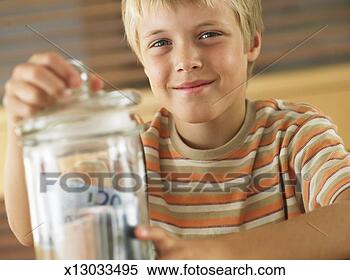 Stock Image - boy (7-9) closing 
lid on jar of 
money, smiling, 
portrait, close-up. 
fotosearch - search 
stock photos, 
pictures, images, 
and photo clipart