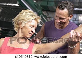 Stock Photograph - mature man stretching 
mature woman's 
arm in gym, smiling. 
fotosearch - search 
stock photos, 
pictures, images, 
and photo clipart