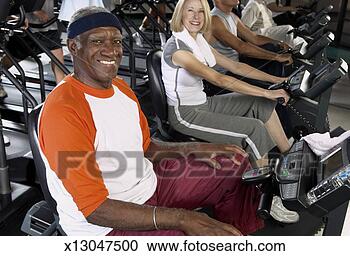 Stock Photography - senior man and 
senior woman on 
bicycles in gym, 
smiling, portrait. 
fotosearch - search 
stock photos, 
pictures, images, 
and photo clipart