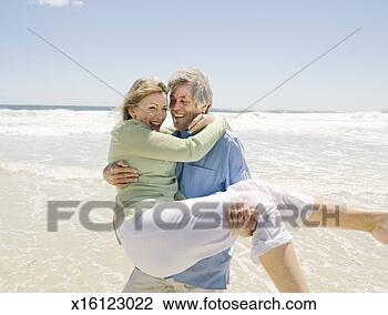 Stock Photo - mature man carrying 
mature woman on 
beach, smiling. 
fotosearch - search 
stock photos, 
pictures, images, 
and photo clipart