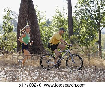 Stock Photography - mature woman jogging 
on dirt track 
behind mature 
man riding bicycle. 
fotosearch - search 
stock photos, 
pictures, images, 
and photo clipart