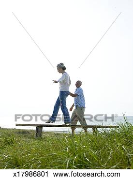 Stock Photography - senior man helping 
senior woman walking 
on bench on coast. 
fotosearch - search 
stock photos, 
pictures, images, 
and photo clipart