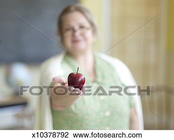Stock Photo - mature female 
teacher holding 
out apple in hand 
(focus on apple). 
fotosearch - search 
stock photos, 
pictures, images, 
and photo clipart