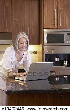 Stock Photo - mature woman using 
laptop on kitchen 
counter. fotosearch 
- search stock 
photos, pictures, 
images, and photo 
clipart
