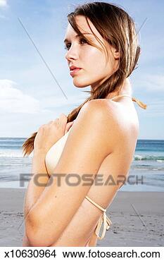 Stock Photo - young brunette 
female wearing 
bikini standing 
on beach,  holding. 
fotosearch - search 
stock photos, 
pictures, images, 
and photo clipart