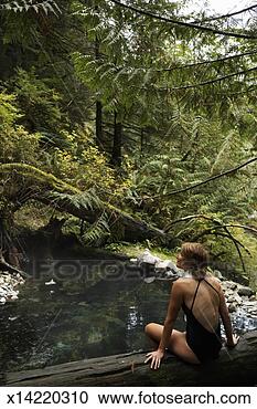 Stock Photography - young woman sitting 
on tree trunk 
by hot spring, 
rear view. fotosearch 
- search stock 
photos, pictures, 
images, and photo 
clipart