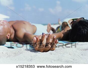 Stock Photo - couple lying on 
beach holding 
hands (focus on 
hands). fotosearch 
- search stock 
photos, pictures, 
images, and photo 
clipart