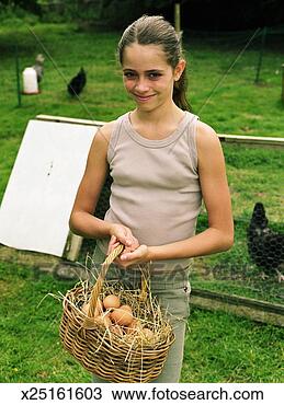 Girl (10-12) by chicken coop holding basket of eggs, smiling, portrait 
