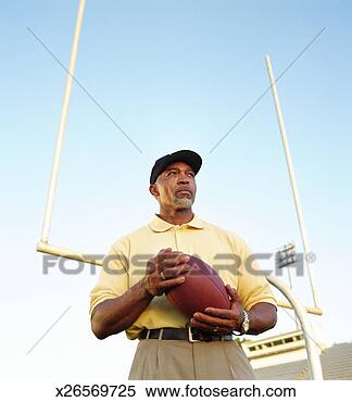 Stock Image - football coach 
holding football, 
standing in front 
of goal post. 
fotosearch - search 
stock photos, 
pictures, images, 
and photo clipart