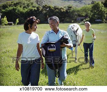 Stock Photography - three mature women 
in field, one 
carrying saddle, 
one leading horse. 
fotosearch - search 
stock photos, 
pictures, images, 
and photo clipart
