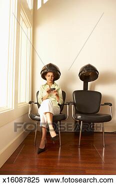 Stock Image - young woman sitting 
under hair dryer 
in hair salon, 
using palmtop. 
fotosearch - search 
stock photos, 
pictures, images, 
and photo clipart