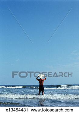 Stock Photography - man standing in 
surf, carrying 
surfboard on head, 
rear view. fotosearch 
- search stock 
photos, pictures, 
images, and photo 
clipart