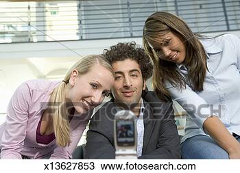 Stock Photo - man and two female 
colleagues looking 
at camera phone, 
smiling. fotosearch 
- search stock 
photos, pictures, 
images, and photo 
clipart