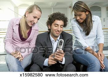 Stock Photography - man and two female 
colleagues looking 
at camera phone, 
smiling. fotosearch 
- search stock 
photos, pictures, 
images, and photo 
clipart