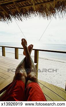 Stock Photograph - man sitting on 
balcony of hut 
beside ocean, 
feet on table, 
low section. fotosearch 
- search stock 
photos, pictures, 
images, and photo 
clipart