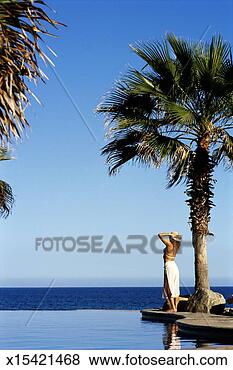 Stock Photo - woman standing 
by pool, looking 
at sea, rear view. 
fotosearch - search 
stock photos, 
pictures, images, 
and photo clipart