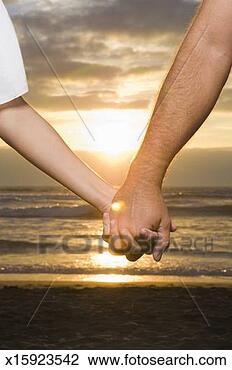 Stock Photo - couple holding 
hands on beach 
at sunset, close-up 
of hands. fotosearch 
- search stock 
photos, pictures, 
images, and photo 
clipart