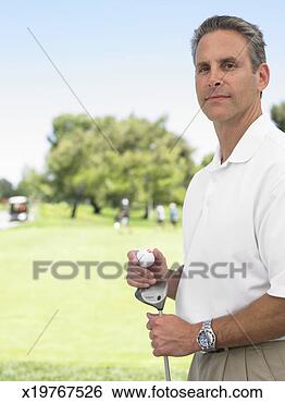 Stock Photo - golfer holding 
club and golf 
ball standing 
on golf course, 
portrait. fotosearch 
- search stock 
photos, pictures, 
images, and photo 
clipart