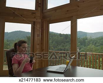 Stock Photo - mature woman sitting 
at desk, holding 
mug, reading from 
laptop. fotosearch 
- search stock 
photos, pictures, 
images, and photo 
clipart