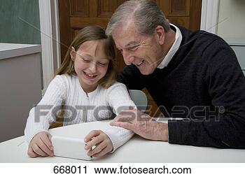 Arquivo de Fotografia - neta,  usando, 
 eletrônico,  
dispositivo,  
enquanto,  avô, 
 relógio. fotosearch 
- busca de fotos, 
imagens e clipart