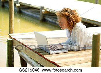 Stock Photo - red-haired woman 
lying on a jetty 
in front of her 
computer. fotosearch 
- search stock 
photos, pictures, 
images, and photo 
clipart