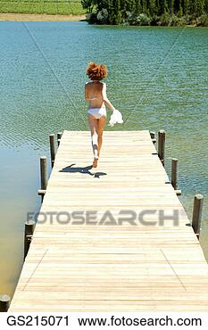 Stock Photography - woman on a jetty, 
running towards 
the water, getting 
undressed. fotosearch 
- search stock 
photos, pictures, 
images, and photo 
clipart