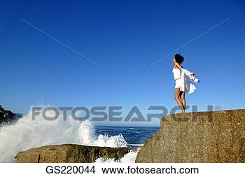 Stock Photo - woman standing 
on a rock, facing 
the sea. fotosearch 
- search stock 
photos, pictures, 
images, and photo 
clipart