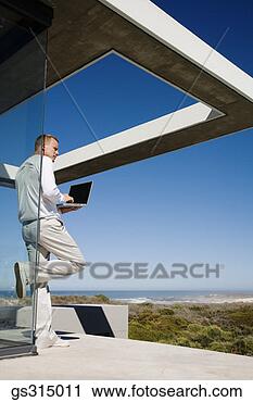 Stock Photography - man with laptop 
leaning against 
glass wall. fotosearch 
- search stock 
photos, pictures, 
images, and photo 
clipart