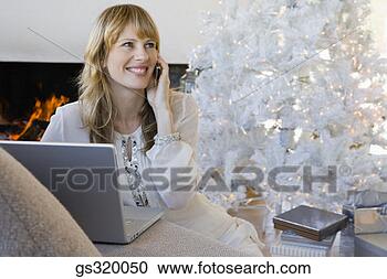 Stock Photography - woman  using laptop 
and cell phone 
by christmas tree. 
fotosearch - search 
stock photos, 
pictures, images, 
and photo clipart