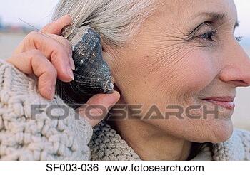 Stock Photo - senior woman holding 
a shell to her 
ear. fotosearch 
- search stock 
photos, pictures, 
images, and photo 
clipart
