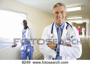 Stock Photograph - mature male doctor 
standing in hospital 
corridor,  smiling, 
 young. fotosearch 
- search stock 
photos, pictures, 
images, and photo 
clipart