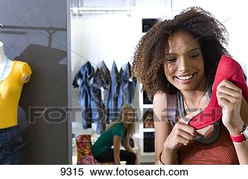 Stock Image - young woman shopping 
in clothes store, 
 holding up high 
heel. fotosearch 
- search stock 
photos, pictures, 
images, and photo 
clipart