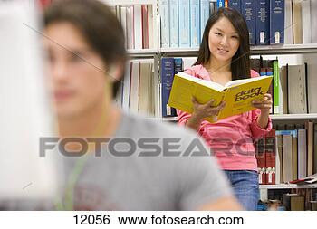 Stock Photo - young man at computer 
in library by 
woman reading 
book by shelf. 
fotosearch - search 
stock photos, 
pictures, images, 
and photo clipart