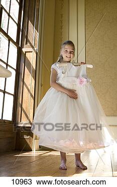 Stock Photo - girl (10-12) holding 
up flower girl 
dress by windows, 
 smiling. fotosearch 
- search stock 
photos, pictures, 
images, and photo 
clipart
