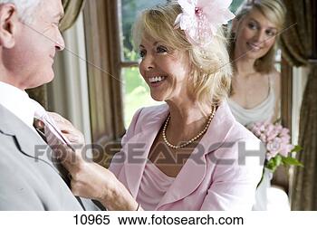 Stock Image - mature woman adjusting 
husband's tie, 
 bride in background, 
 smiling. fotosearch 
- search stock 
photos, pictures, 
images, and photo 
clipart