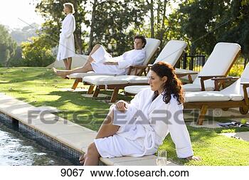 Picture - young woman wearing 
white robe sitting 
by swimming pool 
with legs in. 
fotosearch - search 
stock photos, 
pictures, images, 
and photo clipart