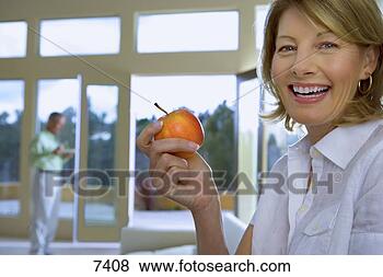 Stock Photo - mature woman eating 
apple at home, 
 senior man in 
background,  focus. 
fotosearch - search 
stock photos, 
pictures, images, 
and photo clipart
