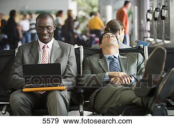 Stock Photograph - two businessmen 
sitting in airport 
terminal,  one 
man using laptop. 
fotosearch - search 
stock photos, 
pictures, images, 
and photo clipart