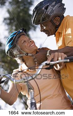 Stock Photo - active senior 
couple preparing 
to cycle in park, 
 man adjusting. 
fotosearch - search 
stock photos, 
pictures, images, 
and photo clipart