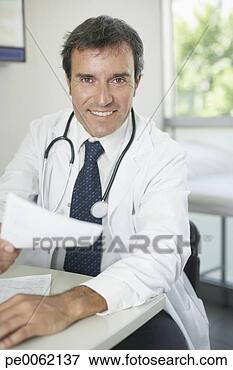 Picture - doctor sitting 
in office with 
paperwork smiling. 
fotosearch - search 
stock photos, 
pictures, images, 
and photo clipart