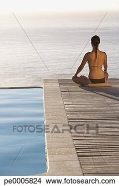 Stock Photo - woman sitting 
on infinity pool 
deck doing yoga 
rear view. fotosearch 
- search stock 
photos, pictures, 
images, and photo 
clipart