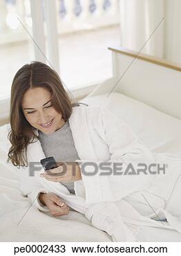 Stock Photo - woman in bathrobe 
reclining on bed 
and texting on 
mobile phone. 
fotosearch - search 
stock photos, 
pictures, images, 
and photo clipart