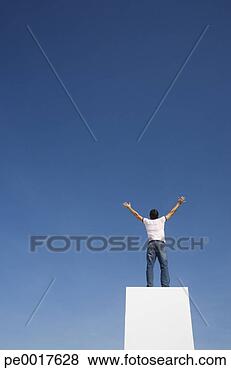 Stock Photo - man standing on 
pedestal or wall 
with arms up and 
blue sky. fotosearch 
- search stock 
photos, pictures, 
images, and photo 
clipart
