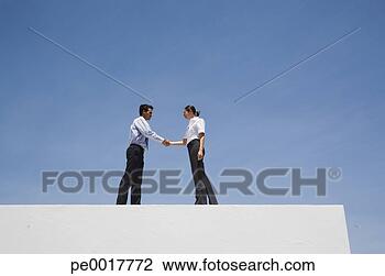 Stock Photo - businessman and 
woman shaking 
hands on wall 
outdoors with 
blue sky. fotosearch 
- search stock 
photos, pictures, 
images, and photo 
clipart