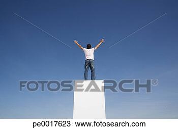 Stock Photo - man standing on 
pedestal or wall 
with arms up and 
blue sky. fotosearch 
- search stock 
photos, pictures, 
images, and photo 
clipart